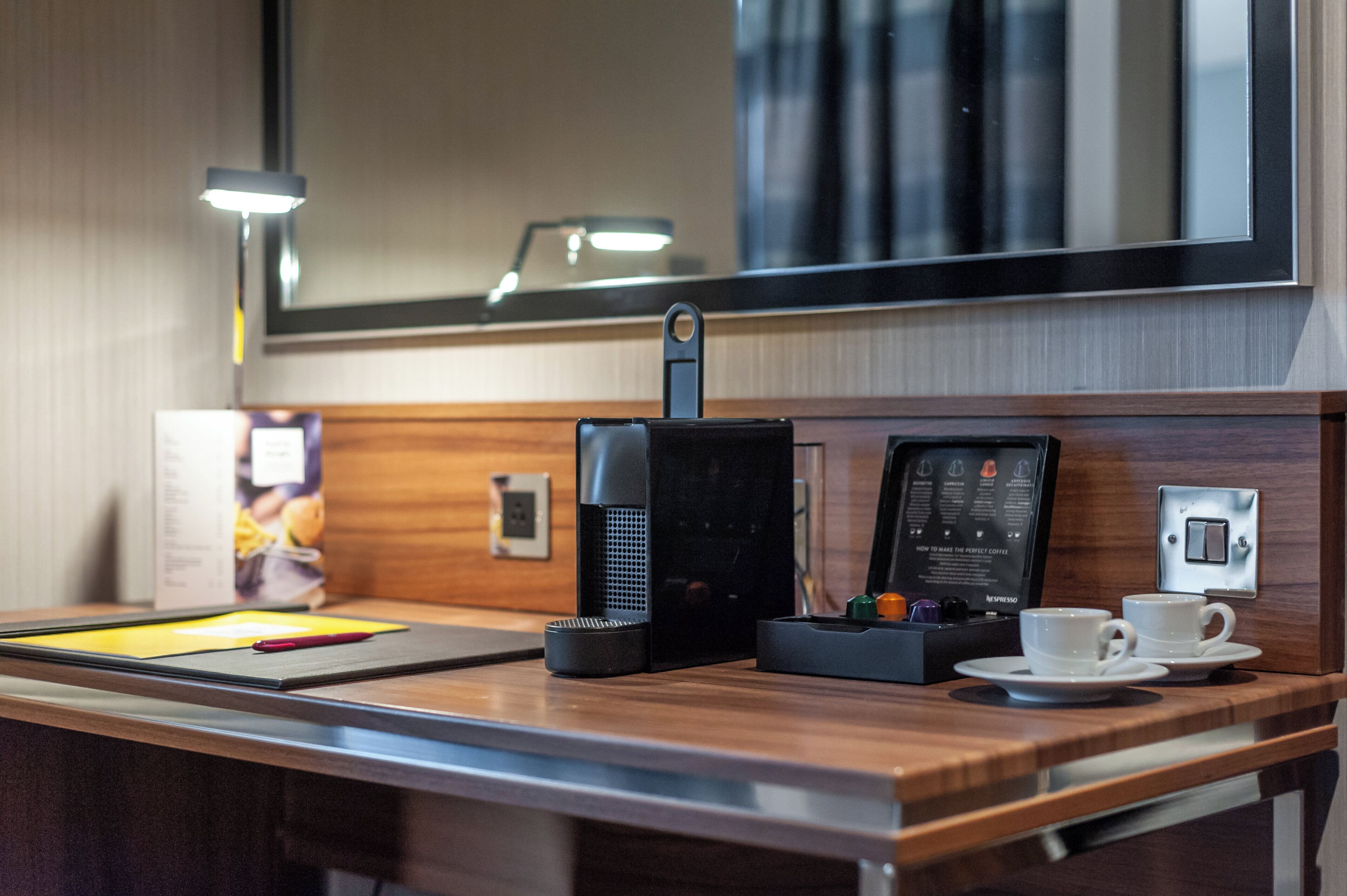A hotel room's kitchenette with a coffee machine, a cup of coffee, and a menu on the counter.