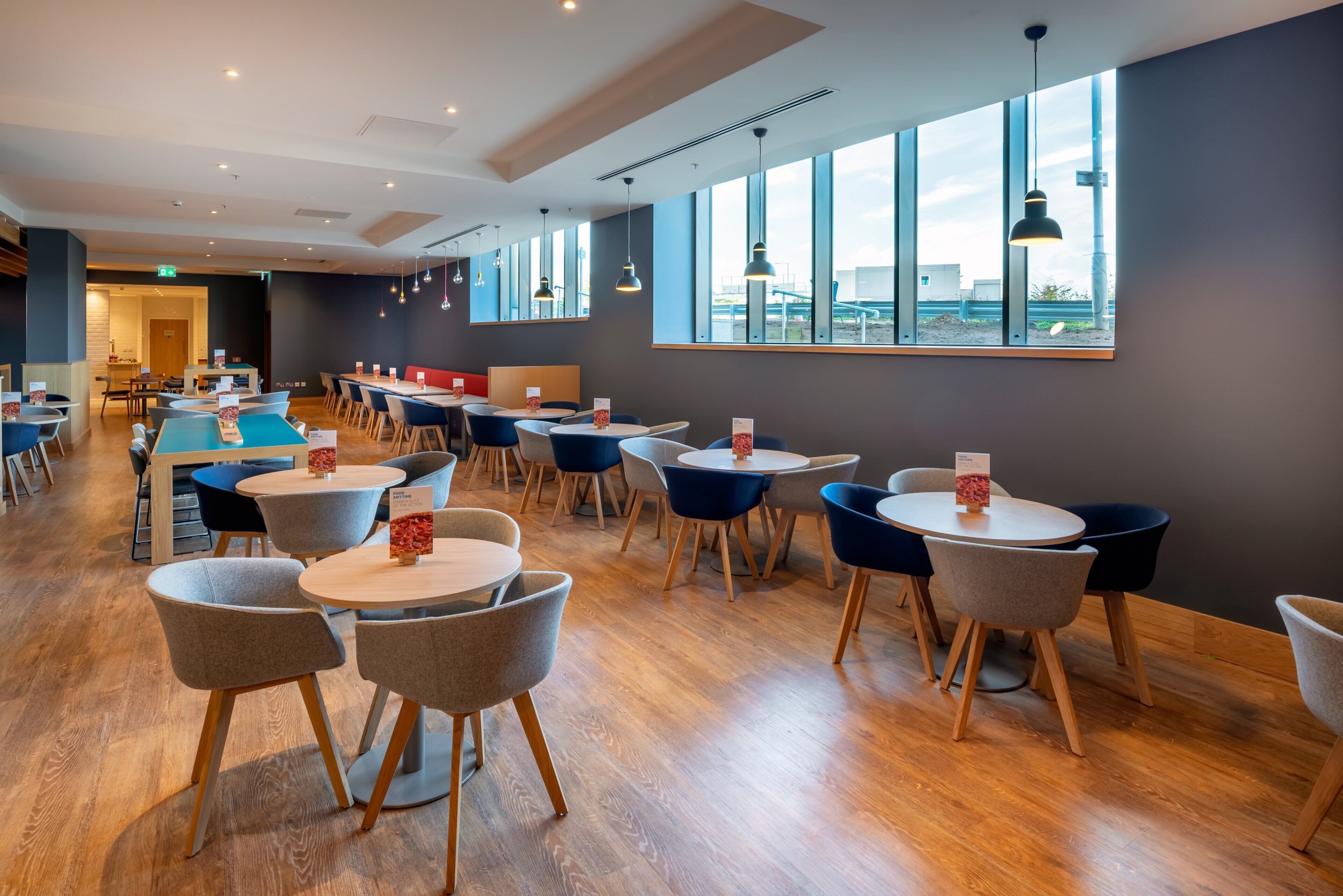 A modern dining area with round tables and chairs, large windows, and pendant lighting.
