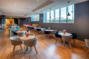 A modern dining area with round tables and chairs, large windows, and pendant lighting. - Holiday Inn Express London Heathrow T4 by IHG (Hounslow)
