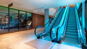 A modern interior with two escalators, glass walls, and a wooden panel wall.