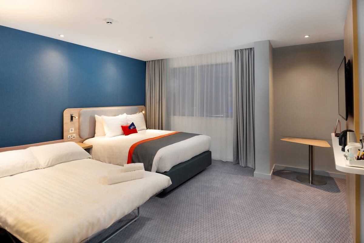A hotel room with two beds, a desk, a chair, a TV, and a window with curtains.