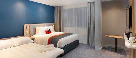 Habitación de hotel con dos camas, un escritorio, una silla, un televisor y una ventana con cortinas.