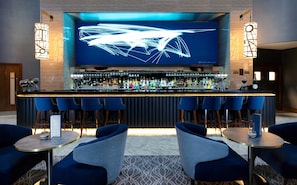 A bar area with a modern design, featuring a long counter, multiple bar stools, and a large screen displaying abstract art.