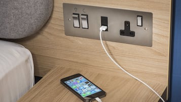 Un teléfono inteligente cargándose sobre una mesita de noche de madera con un enchufe.