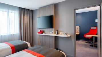 A hotel room with two beds, a TV on the wall, a small desk with a coffee maker, and a red chair.