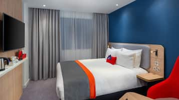 Una habitación de hotel con cama, televisor, escritorio con cafetera y una silla roja.