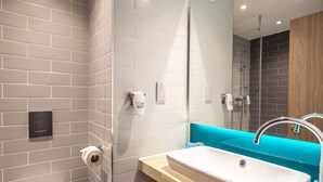 A modern bathroom with grey and white tiles, a white sink, a mirror, and a shower area.