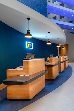 A hotel reception area with multiple wooden reception desks, a blue wall with a starry ceiling design, and a sign for the Holiday Inn Express & Suites.