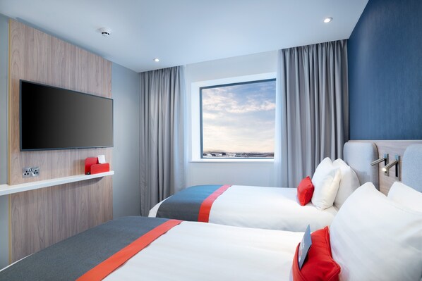 A hotel room with two beds, a flat-screen TV mounted on a wooden panel, a window with curtains, and a view of the landscape. - Holiday Inn Express London Heathrow T4 by IHG (Hounslow)
