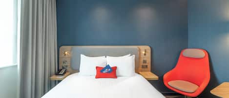 A hotel room with a bed, a red chair, and a nightstand with a phone.