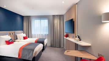 A hotel room with two beds, a desk, a chair, a TV, and a window with curtains.