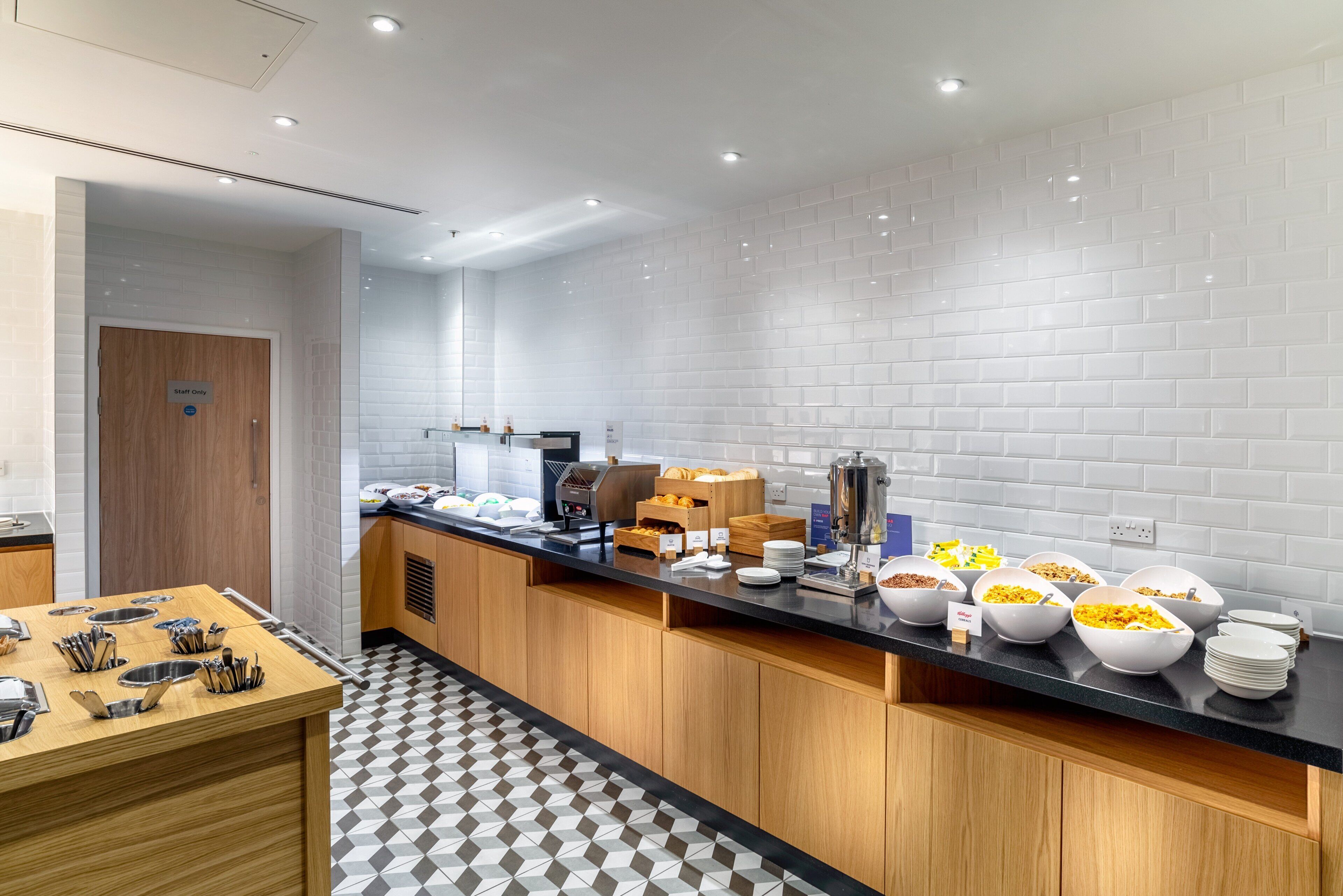 Una cocina moderna con encimera negra, salpicadero blanco con azulejos y suelo con estampado de cuadros.