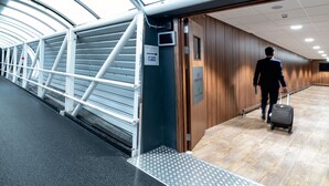 A man in a suit walking with a suitcase in a modern, well-lit corridor with metal railings and wooden walls.