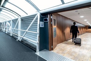 A man in a suit walking with a suitcase in a modern, well-lit corridor with metal railings and wooden walls. - Holiday Inn Express London Heathrow T4 by IHG (Hounslow)