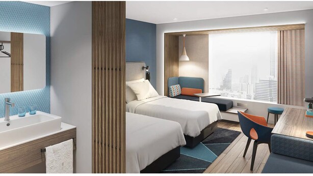 Een moderne hotelkamer met twee bedden, een bureau en een groot raam met uitzicht op de stad.