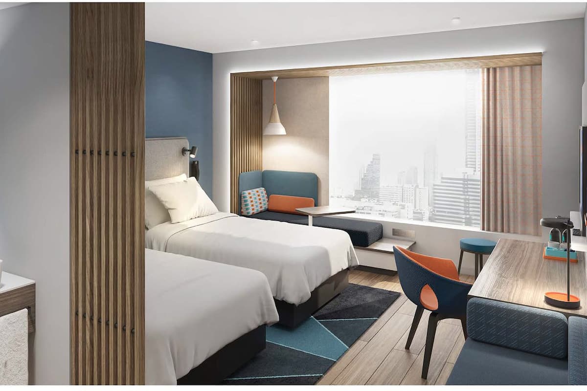 Une chambre d’hôtel moderne avec deux lits, un bureau et une grande fenêtre donnant sur la ville.