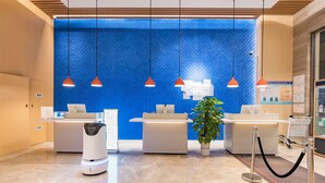 Un espace d’accueil d’hôtel avec un mur orné d’un motif à chevrons bleus, deux comptoirs d’accueil, un kiosque en libre-service et une plante en pot.