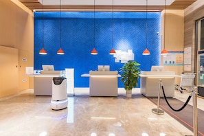 Un espace d’accueil d’hôtel avec un mur orné d’un motif à chevrons bleus, deux comptoirs d’accueil, un kiosque en libre-service et une plante en pot.
