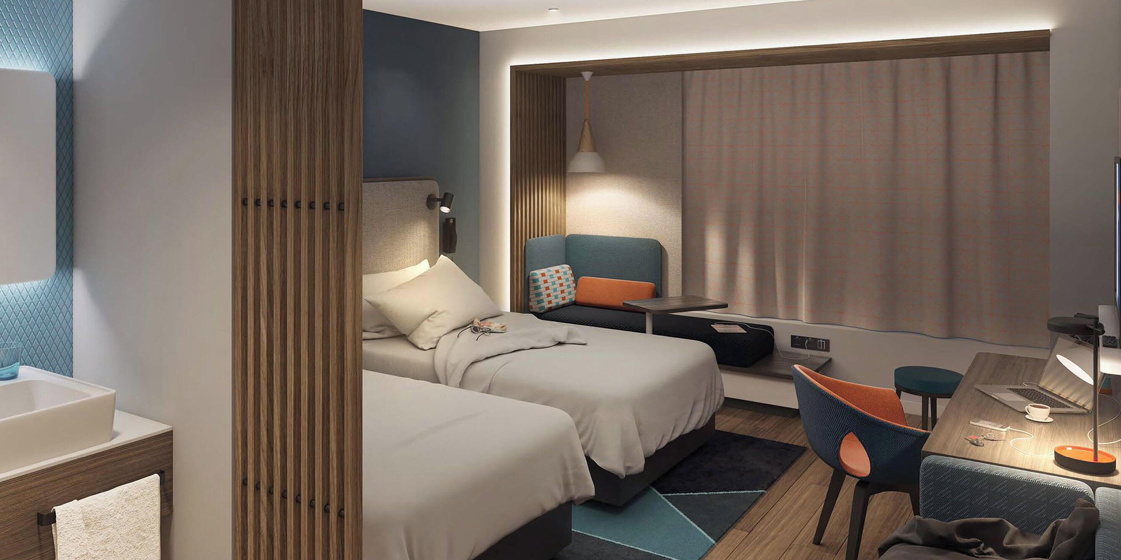 A hotel room with two beds, a desk with a chair, a lamp, and a window with curtains.