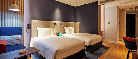 A hotel room with two beds, a desk, a chair, and a hanging light fixture.