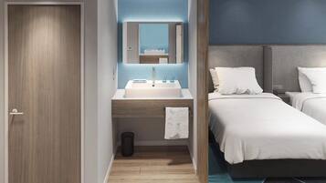 A hotel room with a wooden door, a bathroom with a sink and mirror, and two beds with white bedding.