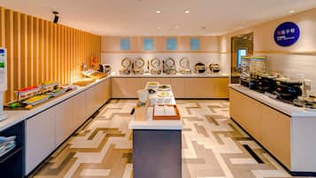 A modern breakfast area with a buffet setup, including various food containers and a coffee machine.