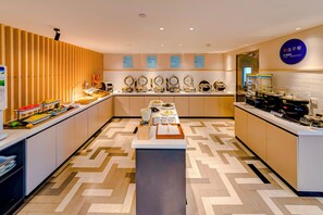 Un espace moderne dédié au petit-déjeuner, avec un buffet proposant divers plats présentés dans des récipients et une machine à café.