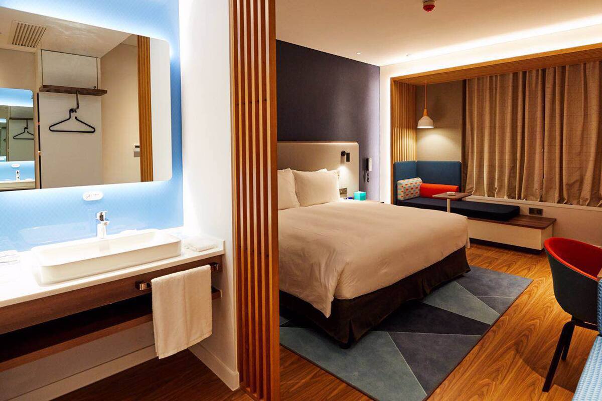 Une chambre d’hôtel moderne dotée d’un grand lit, d’un bureau, d’une chaise, d’une salle de bain avec un lavabo et un miroir, et offrant une vue sur la ville.