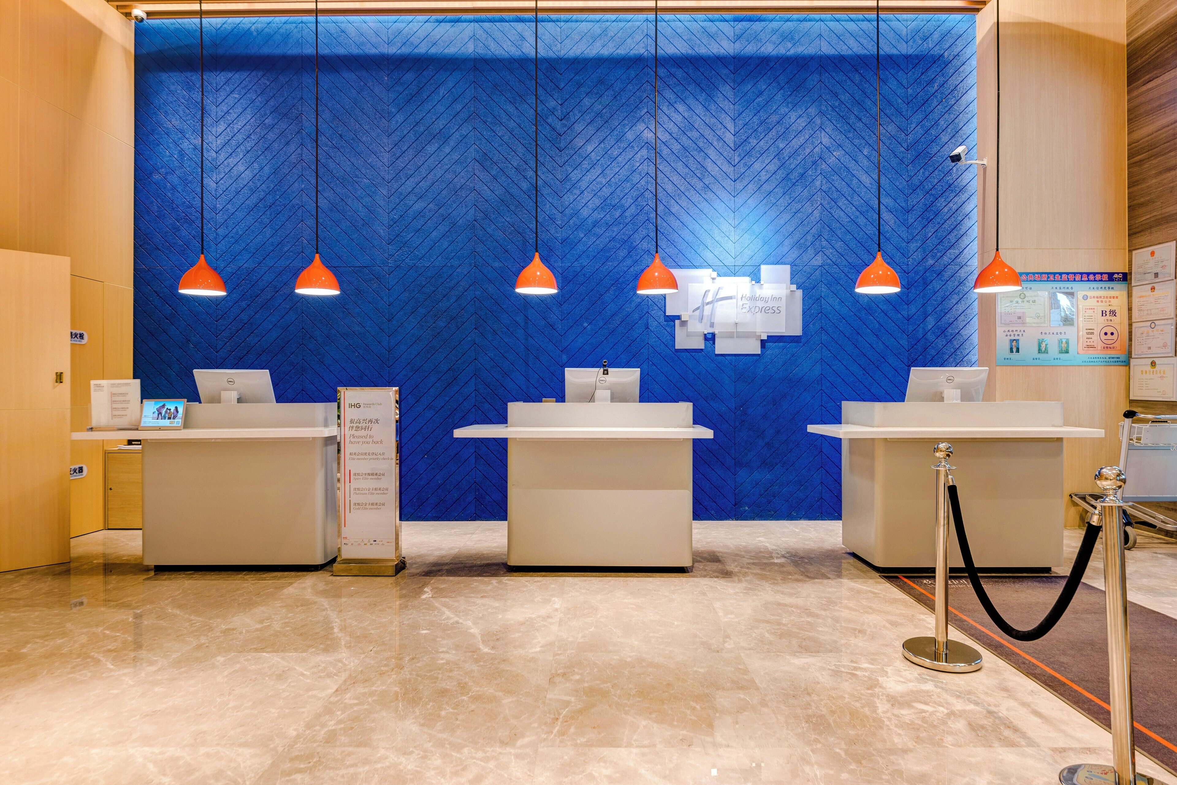 Un área de recepción con tres mostradores, una pared azul con textura y lámparas colgantes naranjas.