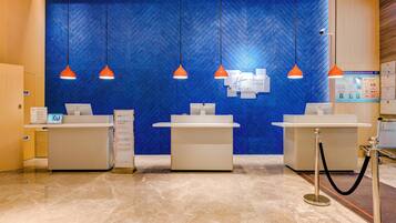 Un área de recepción con tres mostradores, una pared azul con textura y lámparas colgantes naranjas.
