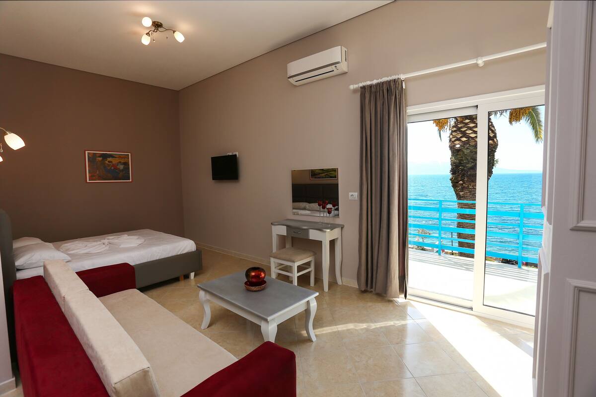 A bedroom with a bed, a desk, a chair, and a view of the sea.