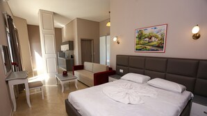 A hotel room with a bed, bedside tables, a desk, a chair, a sofa, a wardrobe, and a painting on the wall. - Serxhio Apartments (Sarandë)