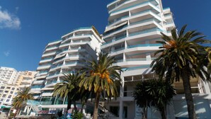 A multi-story hotel with balconies, palm trees, and a clear blue sky. - Serxhio Apartments (Sarandë)