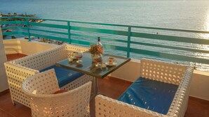 A balcony with wicker furniture, a glass table, and a view of the sea and mountains. - Serxhio Apartments (Sarandë)