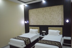 Habitación de hotel con dos camas, un cabecero grande con diseño y lámparas de noche, junto a una mesita con un teléfono.