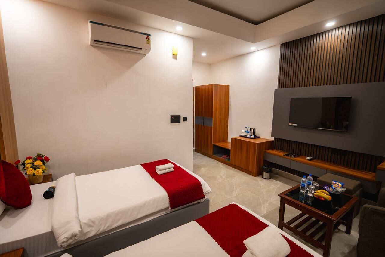 A hotel room with two beds, a TV, a small table with snacks, a wardrobe, and an air conditioning unit.