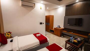 A hotel room with two beds, a TV, a small table with snacks, a wardrobe, and an air conditioning unit.