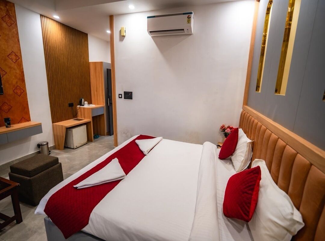 A hotel room with a bed, a desk, a chair, an air conditioning unit, and a mirror.