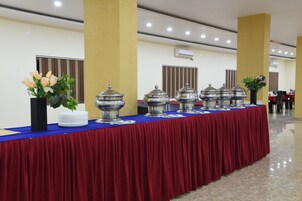A banquet table with a red tablecloth, silver serving dishes, and white plates.