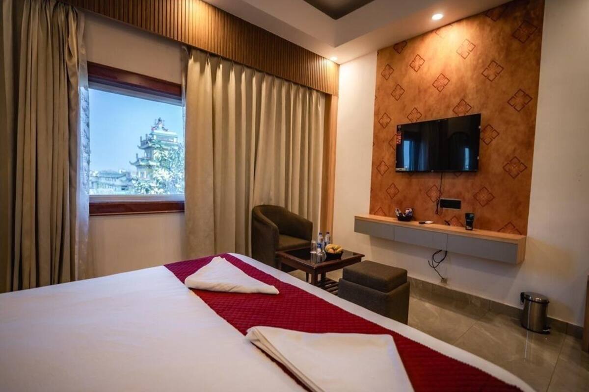 Ein Hotelzimmer mit Bett, Schreibtisch, Stuhl, Fernseher und Blick auf ein Gebäude.