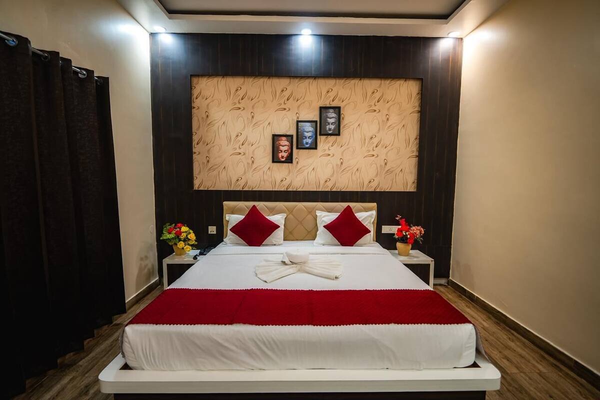 Ein ordentlich gemachtes Bett mit roter Decke, zwei roten Kissen und einem weißen Handtuch. Auf je einem der beiden Nachttische stehen Blumenvasen. Der Raum hat dunkle Holzvertäfelung an den Wänden und eine Deckenleuchte.