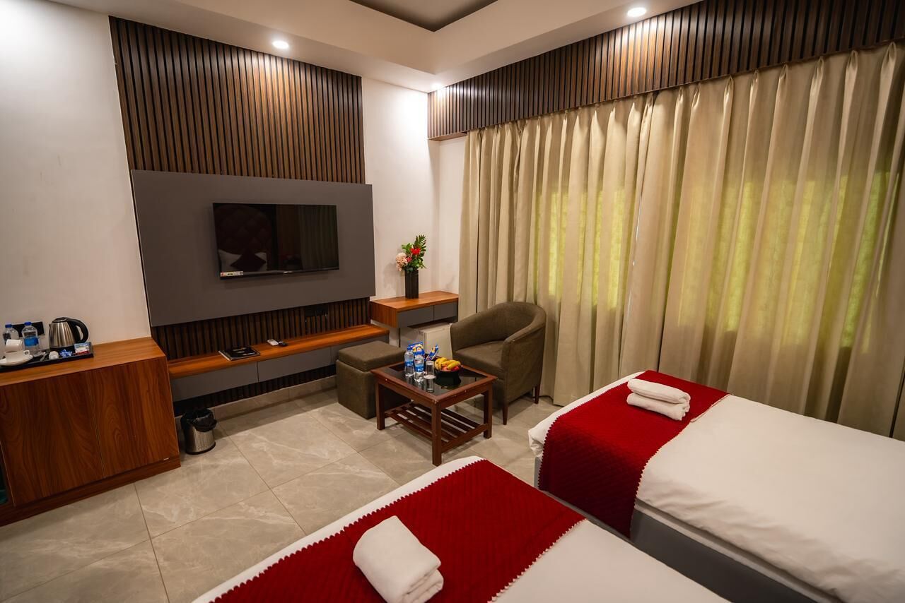 A hotel room with two beds, a TV, a small table with a plant, a chair, and a desk with a computer.