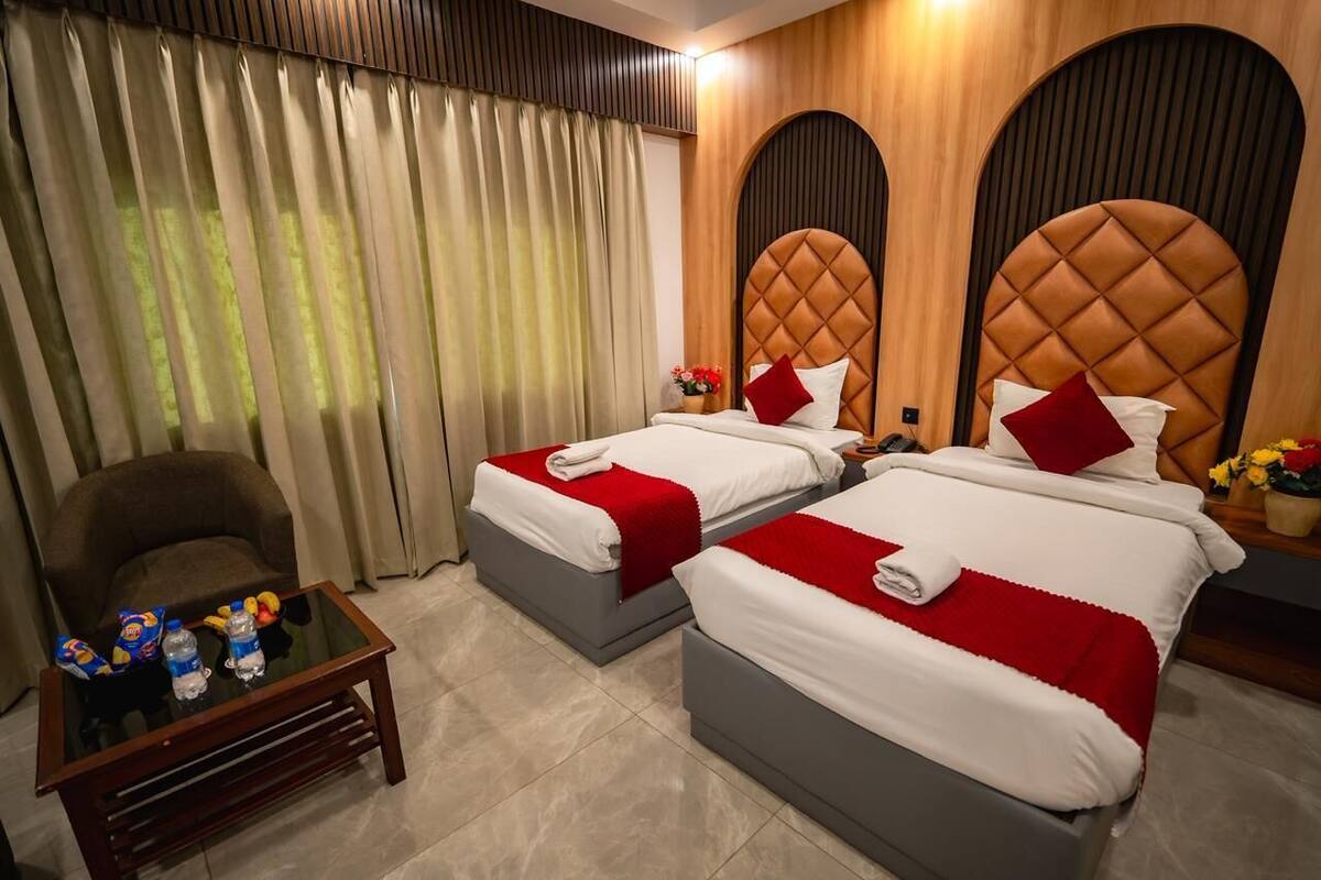 Ein Hotelzimmer mit zwei Betten, einem Sessel, einem kleinen Tisch und Vorhängen.