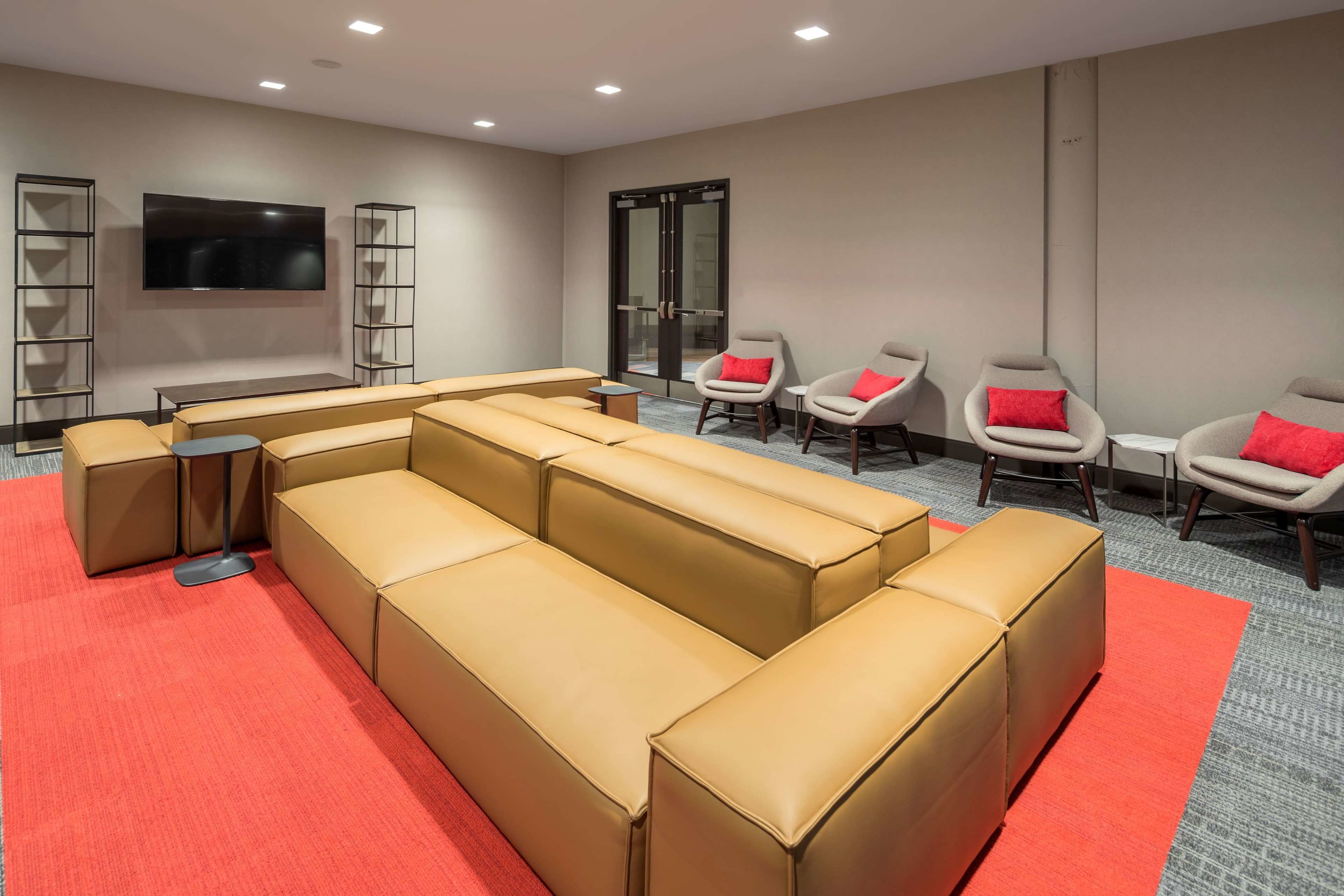 A modern lounge area with a large L-shaped sofa, a flat-screen TV mounted on the wall, and a glass door leading to another room.