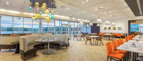 A spacious restaurant with high ceilings, pendant lighting, and large windows offering a view.