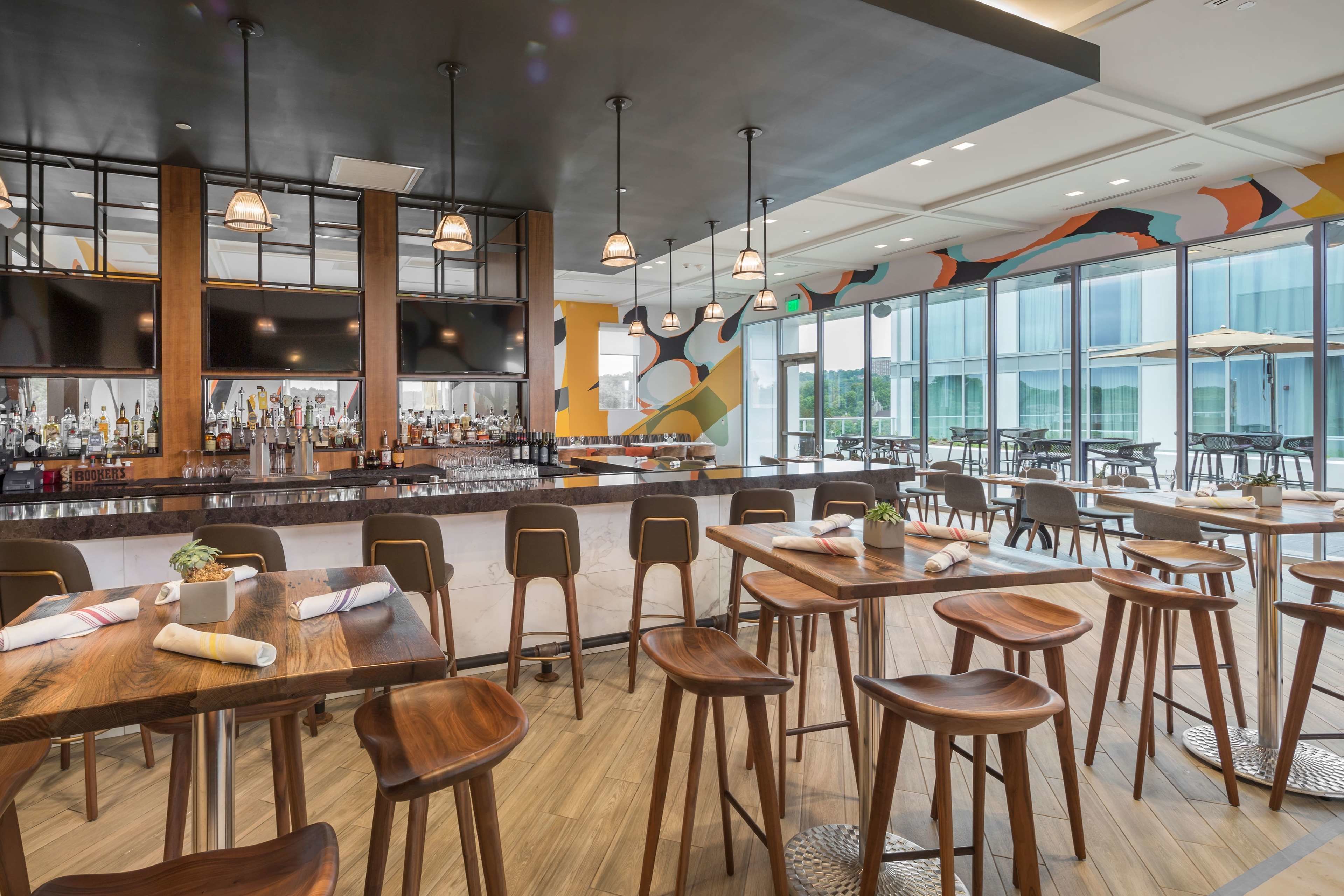 A modern restaurant with a bar area, wooden tables and chairs, and large windows offering a view. - The Summit Hotel (Cincinnati)