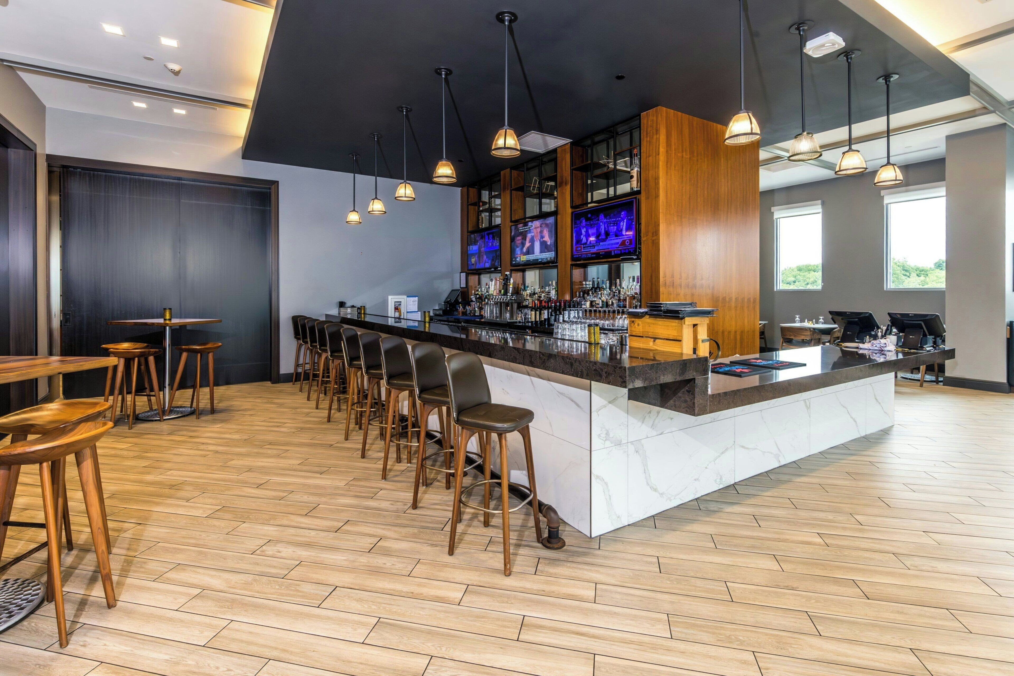 Uma área de bar com um balcão comprido, vários banquetes e uma tela de televisão.