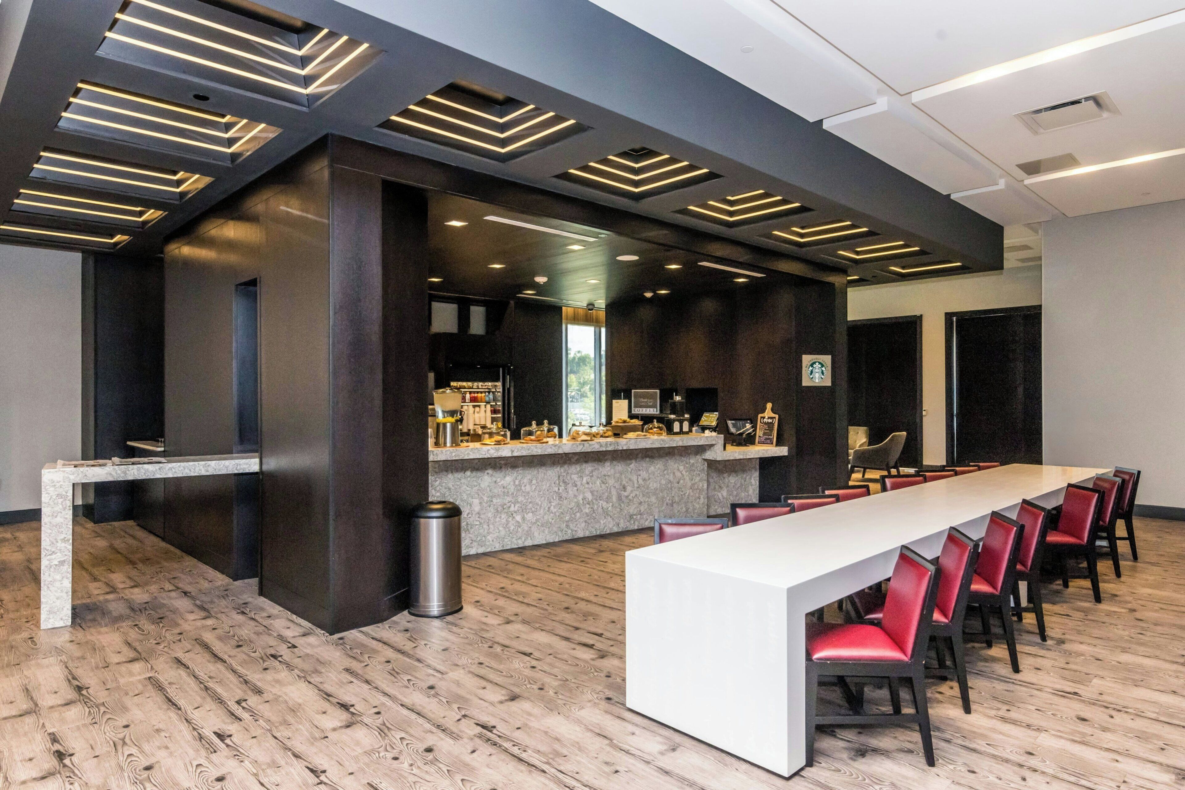 A conference room with a long table, red chairs, a bar area, and modern lighting fixtures.