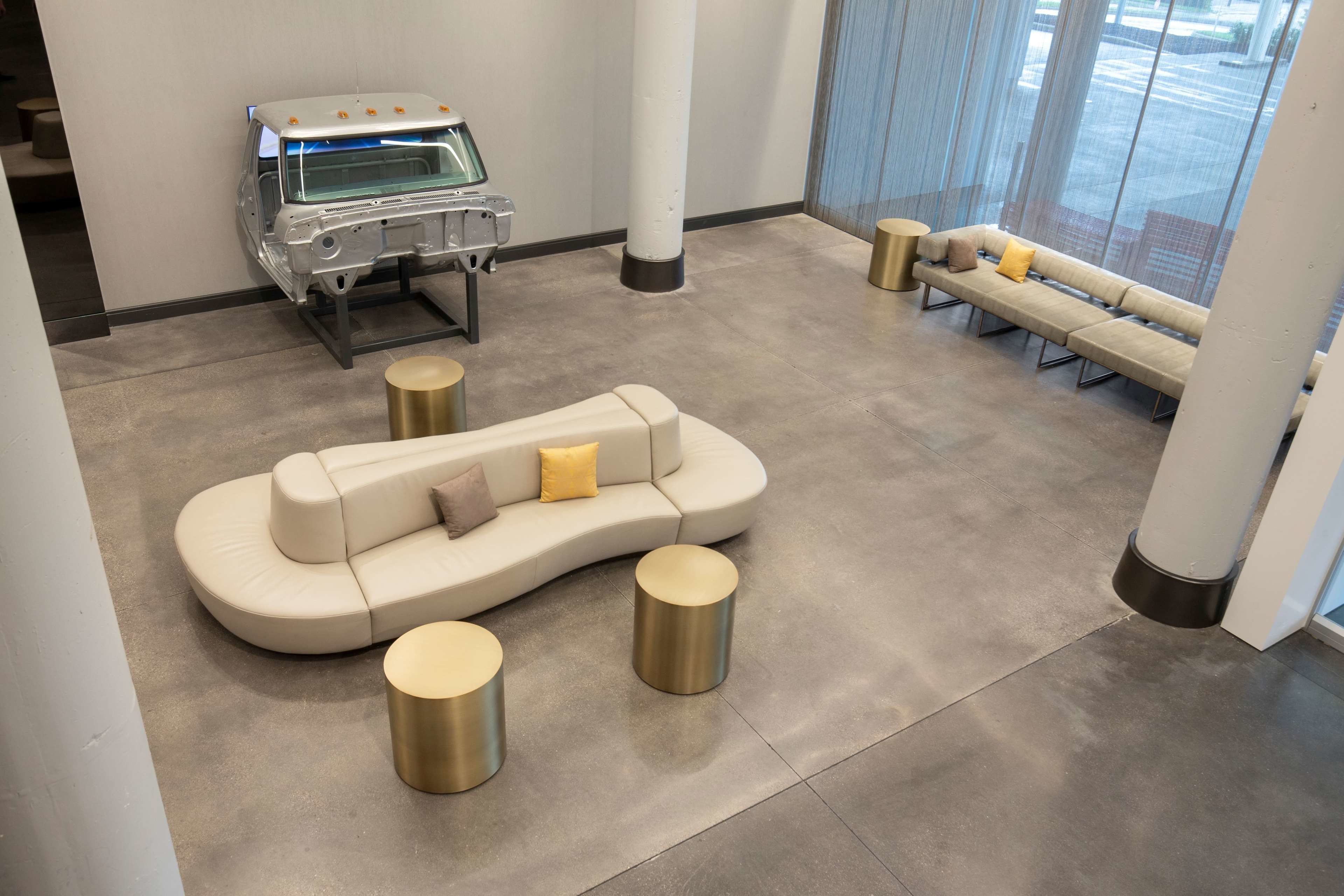 A modern lobby with a curved sofa, two gold round tables, and a car display.
