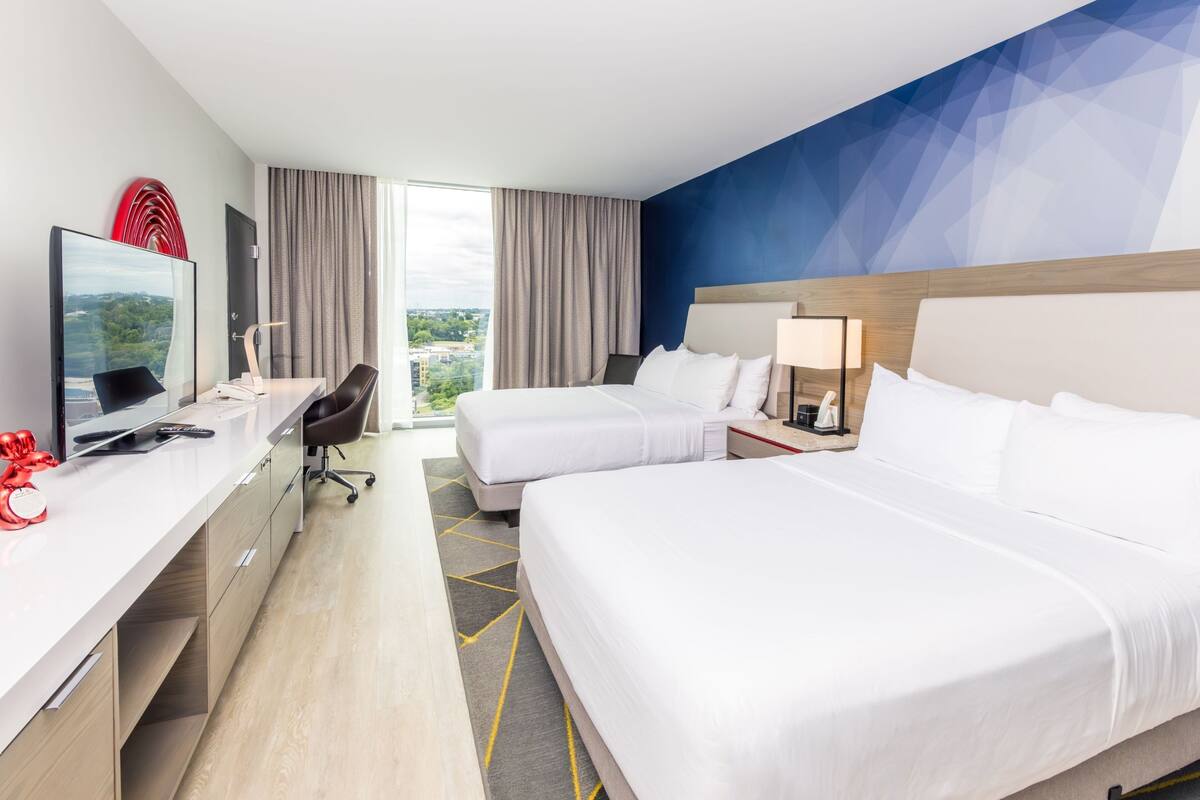 Habitación de hotel con dos camas, un escritorio con computadora, una silla y un televisor.